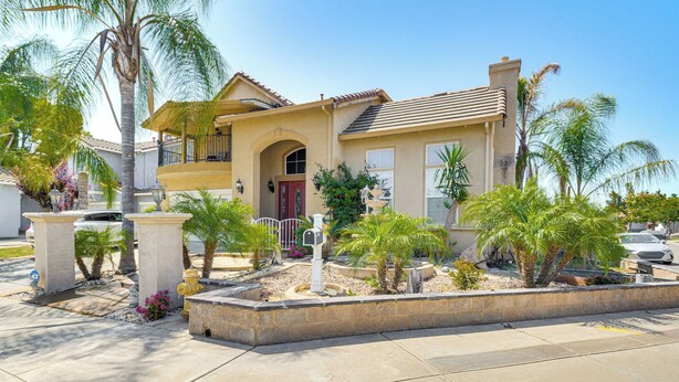 A two-story house with a balcony, surrounded by palm trees and a landscaped garden. - Golf, Fish & More: Cozy ‘Safari Unit’ in Atwater! (Atwater)