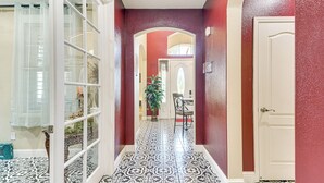 A hallway with patterned floor tiles, a white door, and a red wall. - Golf, Fish & More: Cozy ‘Safari Unit’ in Atwater! (Atwater)