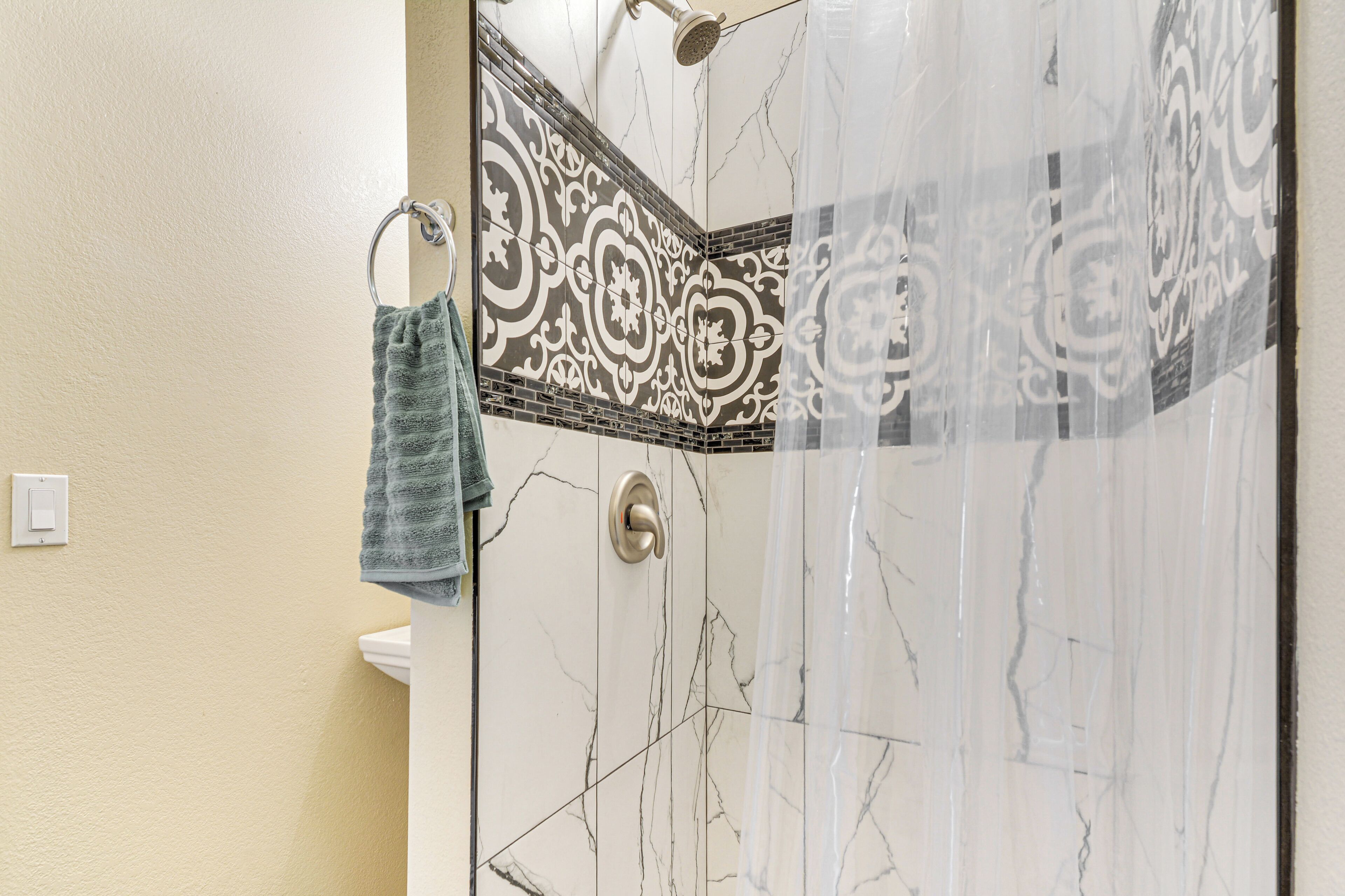 A bathroom with a shower, a towel rack, and a patterned tile backsplash.