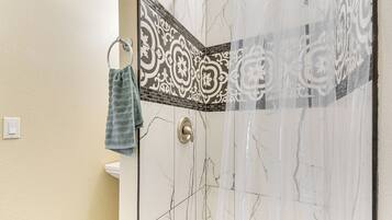 A bathroom with a shower, a towel rack, and a patterned tile backsplash.