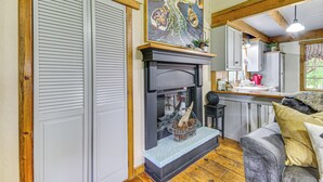 Un interior acogedor con chimenea, vigas de madera, zona de cocina y área de descanso con sofá.