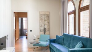 Una sala de estar moderna con un sofá azul, una mesita y un sillón. Hay un cuadro abstracto grande en la pared y una ventana con cortinas.