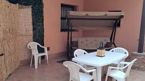 Un espacio de descanso al aire libre con techo, una mesa, sillas, una cama superpuesta y un muro de ladrillo.