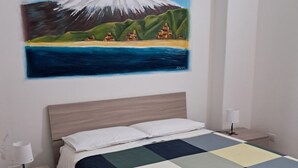 Un dormitorio con cama, mesitas de noche, una lámpara, un cuadro de una montaña y vistas al mar.