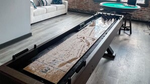 Una habitación con mesa de billar, sofá y grandes ventanales con vistas a la calle.