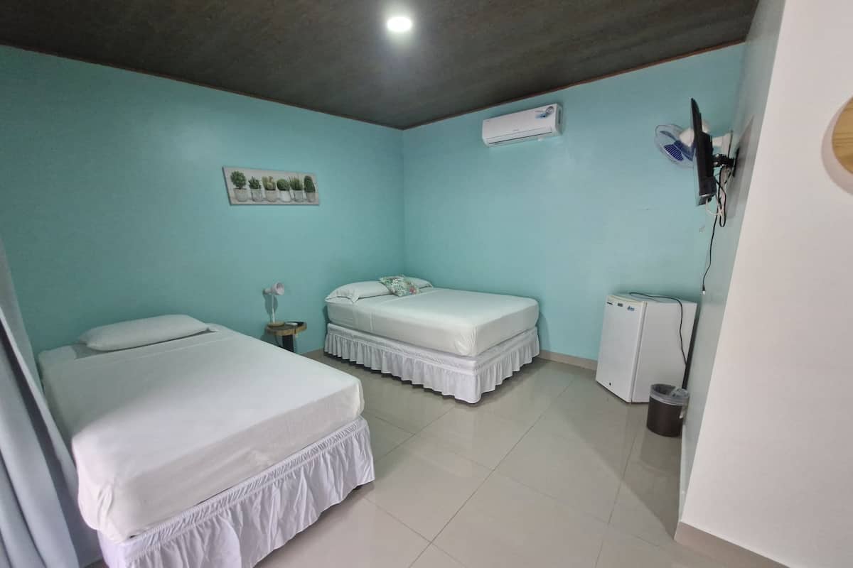Een kamer met twee bedden, een wandairconditioner, een klein tafeltje met een lamp en een prullenbak.