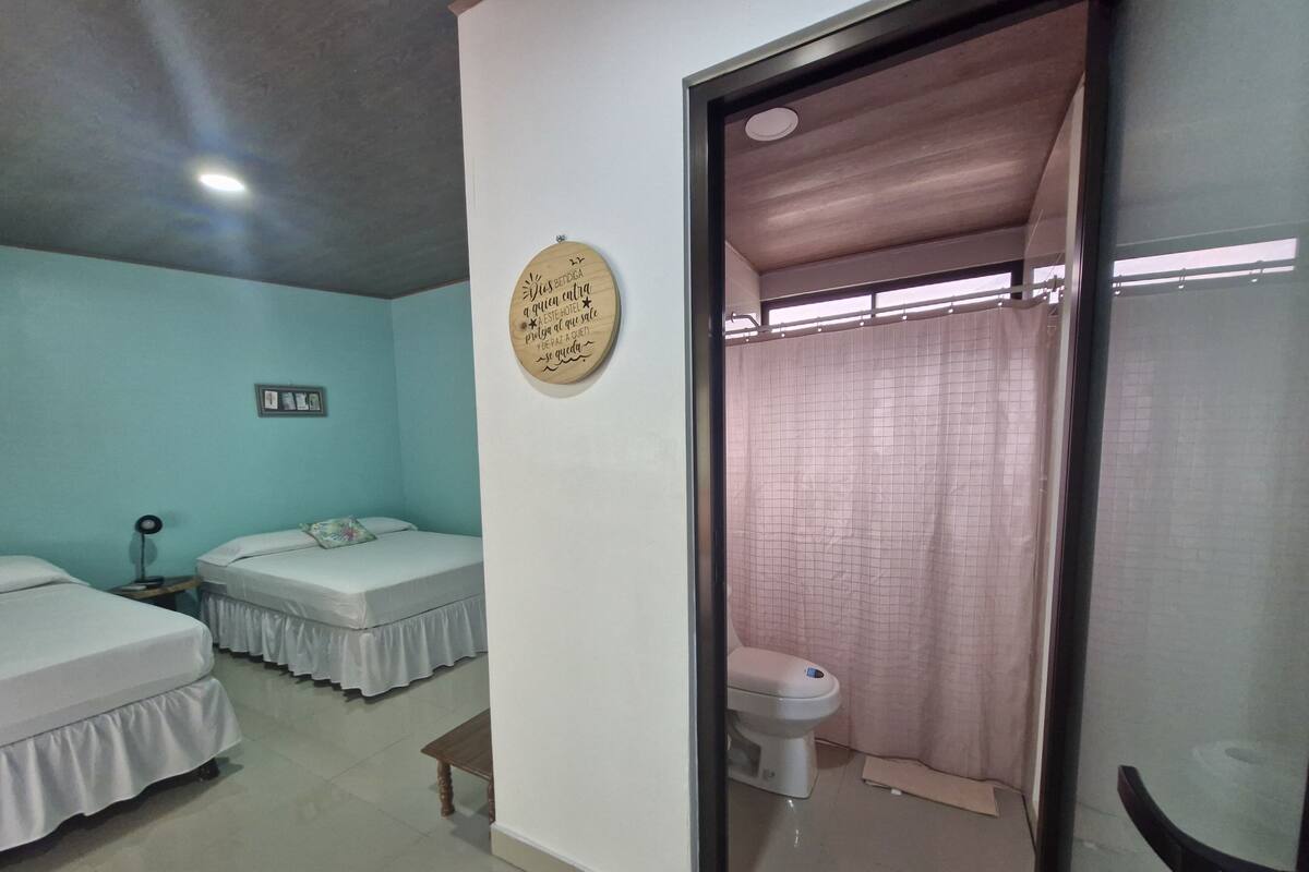 Een hotelkamer met twee bedden, een klein tafeltje, een bedlampje, een toilet en een douchegordijn.