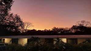 Un hôtel doté d’une piscine, entouré d’une végétation luxuriante et offrant une vue sur un ciel au coucher du soleil.