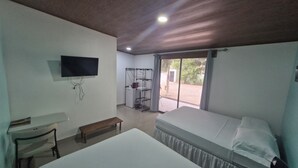 Une chambre d’hôtel avec deux lits, un bureau, une chaise, une télévision et une porte coulissante donnant sur l’extérieur.