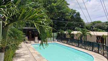 A rectangular swimming pool with a tiled deck, surrounded by a decorative fence and palm trees.