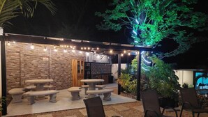 Une terrasse extérieure avec des tables et des chaises en pierre, un mur en pierre et des guirlandes lumineuses.