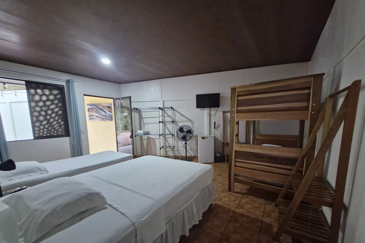 Een kamer met twee bedden, een houten stapelbed, een televisie, een ventilator en een raam met decoratief zonnescherm.