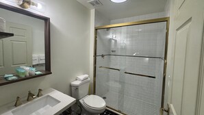 A bathroom with a white sink, toilet, and a glass-enclosed shower with a gold frame. - 2 Bedroom Triple Queen Room - 2QQQS (Gatlinburg)