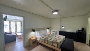 A bedroom with a bed, bedside table, lamp, and a desk with a chair. There is a window with curtains and a view of the outside. - 2 Bedroom Triple Queen Room - 2QQQS (Gatlinburg)