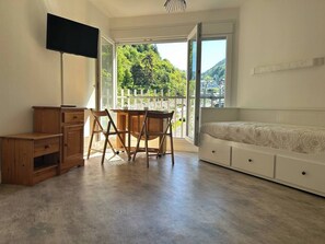 Ein Zimmer mit einem Holztisch, einem Sessel, einem Fernseher, einem Bett und Blick auf Grünflächen sowie einen weißen Zaun.