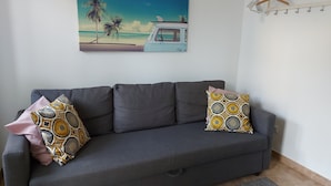 A grey sofa with patterned cushions, a beach-themed painting, and a drying rack. - Central Lisbon Terrace (Lisboa)