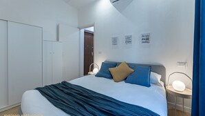 Une chambre à coucher comprenant un lit, une table de chevet et une armoire. Les murs sont décorés et la pièce est équipée d’un climatiseur.