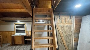 A wooden spiral staircase in a rustic room with wooden walls and a window.