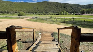 A wooden pathway leading to a fenced area with a view of a forested mountain range.