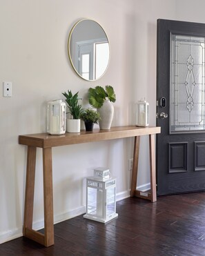 A wooden console table with a mirror above it, flanked by potted plants and a white lantern. - Palm House Luxury Retreat for Families + Corporate (Charlotte)