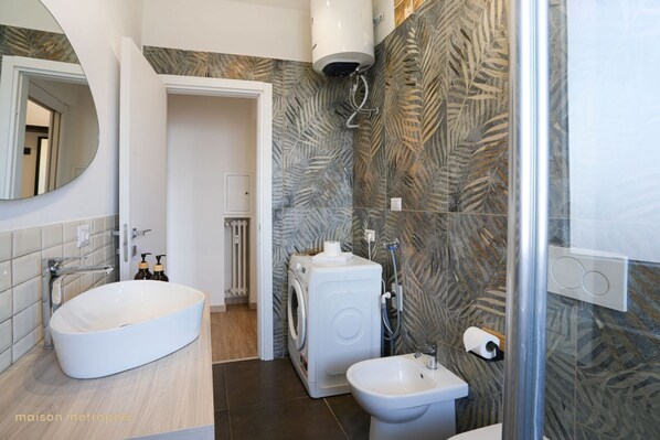 A modern bathroom with a freestanding bathtub, a washing machine, and a bidet. - Torino | Lingotto House | Trilocale con balcone e vista (Torino)