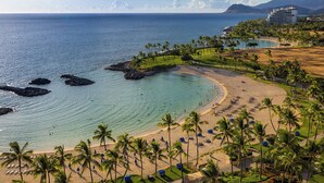 A beach resort with a clear view of the ocean, palm trees, and a hotel in the background.