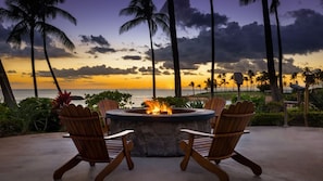 Un hogar con sillas a su alrededor, con vista a una playa con palmeras y un atardecer.