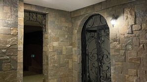 A stone-walled room with a marble floor, a decorative metal door, and a hanging lantern.