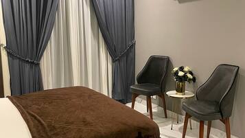 Un dormitorio moderno con una cama, dos sillas, una mesita con flores y un equipo de aire acondicionado en la pared.