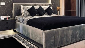 A modern bedroom with a large bed, dark walls, and a wooden wardrobe.