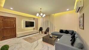 A modern living room with a flat-screen TV, a sofa, a coffee table, and a potted plant.