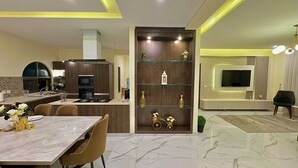 A modern kitchen with a dining area, marble flooring, and a TV in the living room.