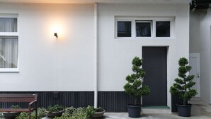 A modern building with a white facade, a dark door, and three windows. There are potted plants and a bench outside. - Torino | Red Oasi Apartment (Torino)