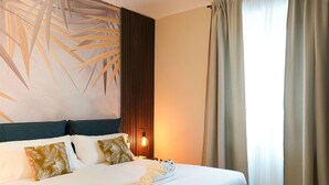 A neatly made bed with white linens and rolled towels, a wall-mounted light fixture, and a large abstract painting. - Torino | Red Oasi Apartment (Torino)