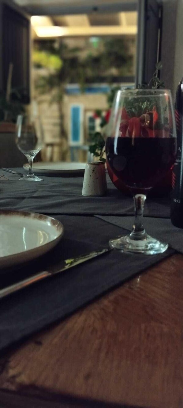 Una mesa de comedor con una copa de vino y un plato, frente a una ventana que ofrece vistas a edificios y zonas verdes.