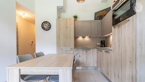 Una cocina moderna con armarios de madera clara, extractor de acero inoxidable y horno empotrado. Hay una mesa de comedor con sillas y un reloj de pared.