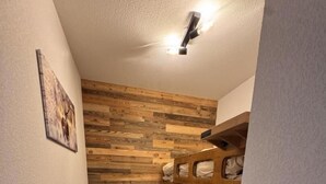 Una habitación pequeña y acogedora con un panel de madera, una litera, un taburete y una puerta.
