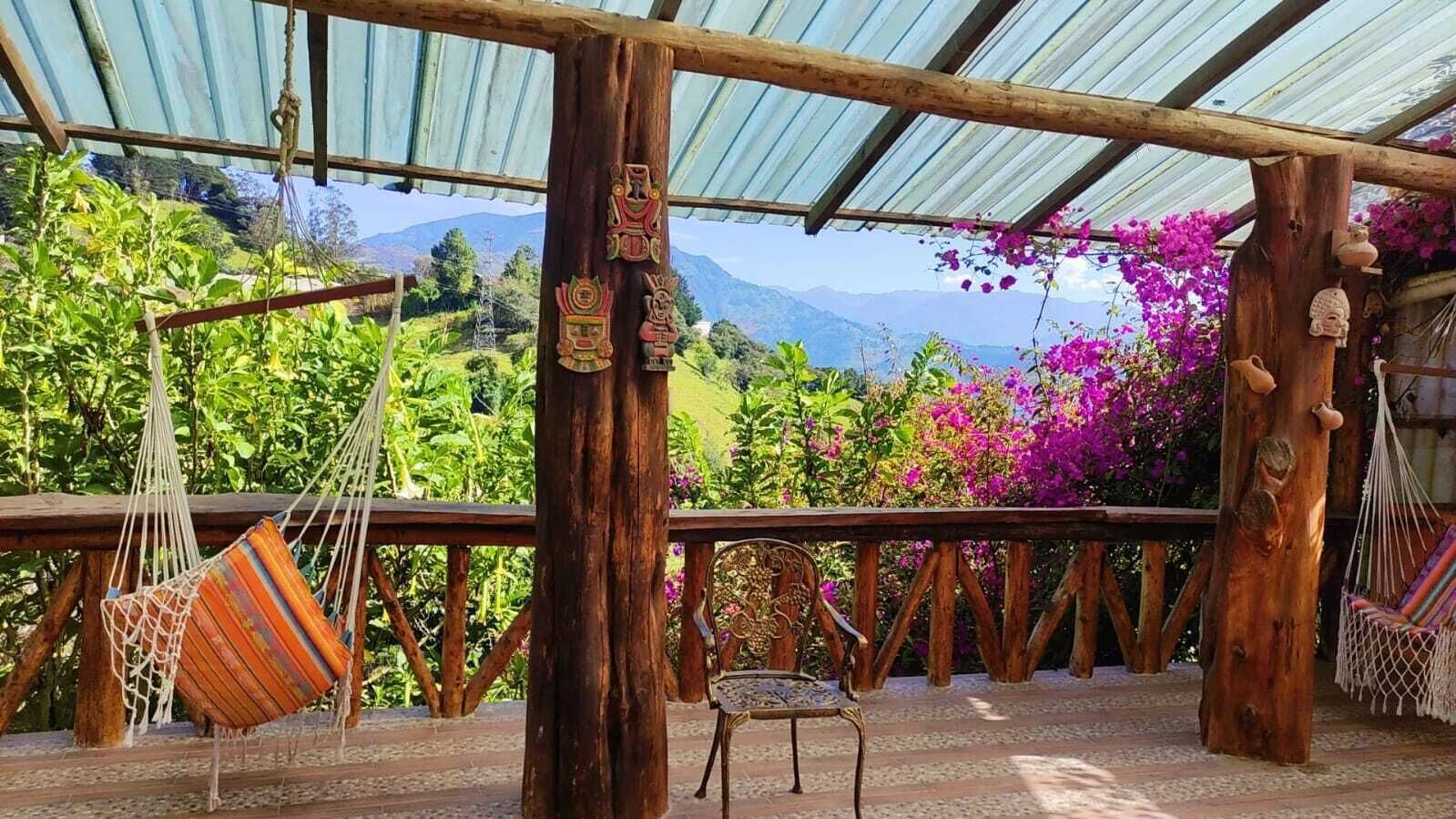 Una terraza de madera con una hamaca, una silla y vistas a montañas y flores.