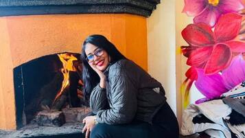 Una persona sentada junto a una chimenea, con un cuadro de flores en la pared.