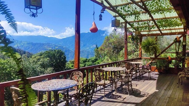 An outdoor patio with tables and chairs, a pergola, and a view of mountains. - Las Orquideas Runtun Lodge (Baños de Agua Santa)