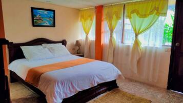 Un dormitorio con cama, mesita de noche, lámpara, un cuadro en la pared y cortinas.