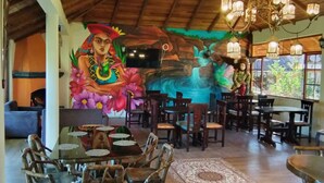 A restaurant with wooden ceiling beams, a mural, and a chandelier. - Las Orquideas Runtun Lodge (Baños de Agua Santa)