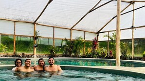 A pool area with a greenhouse structure, surrounded by various plants and a clear sky. - Las Orquideas Runtun Lodge (Baños de Agua Santa)