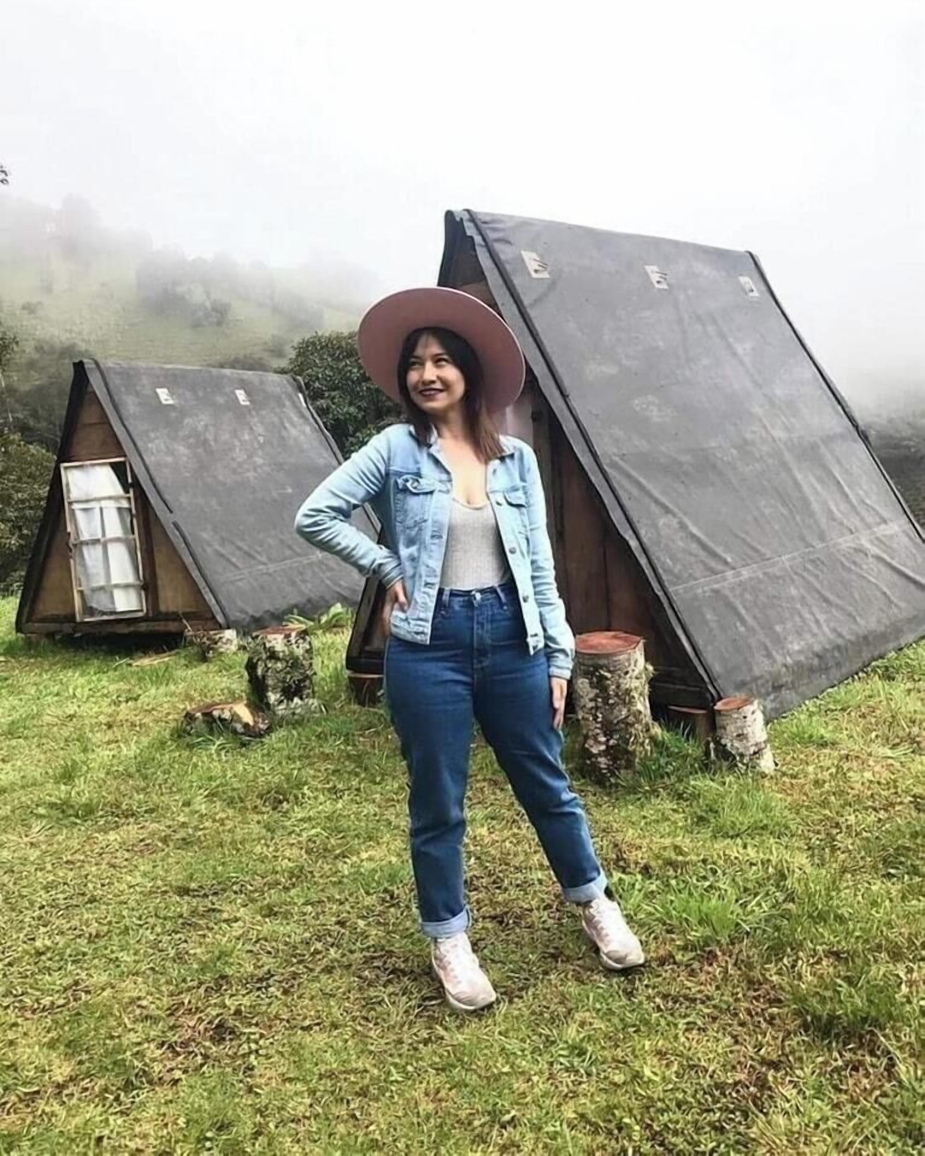 A person standing in front of a tent-like structure with a natural landscape in the background.