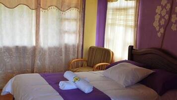 A bedroom with a bed, two chairs, and a window with curtains.
