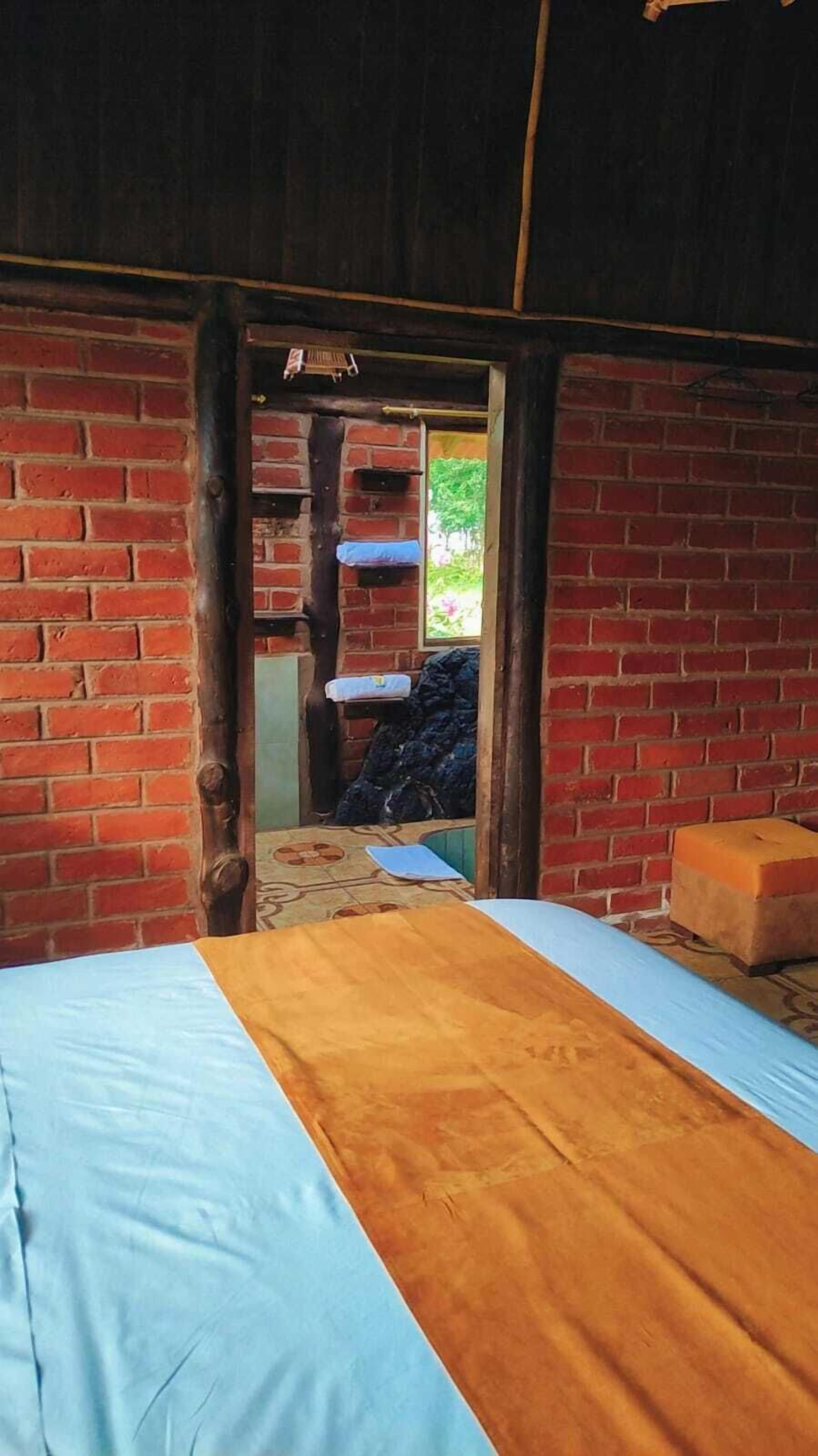Um quarto com uma cama, um banco de madeira e uma parede de tijolos.