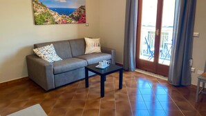 Un salón con un sofá, una mesa de centro y un cuadro de un pueblo costero.