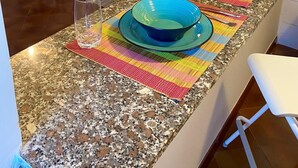 Una cocina con encimeras de granito, una mesa de comedor con platos de colores, un televisor y una silla.