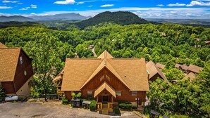 A wooden cabin with a triangular roof, surrounded by dense forest and mountains in the background. - 6 Bedroom VIEW next to Dollywood FLASH SALE today (Sevierville)