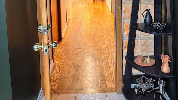 A hallway with wooden flooring, a chair, a shelf with decorative items, and a door with a key lock. - A min walk to the zoo and University!2 bed apartment (Peterborough)